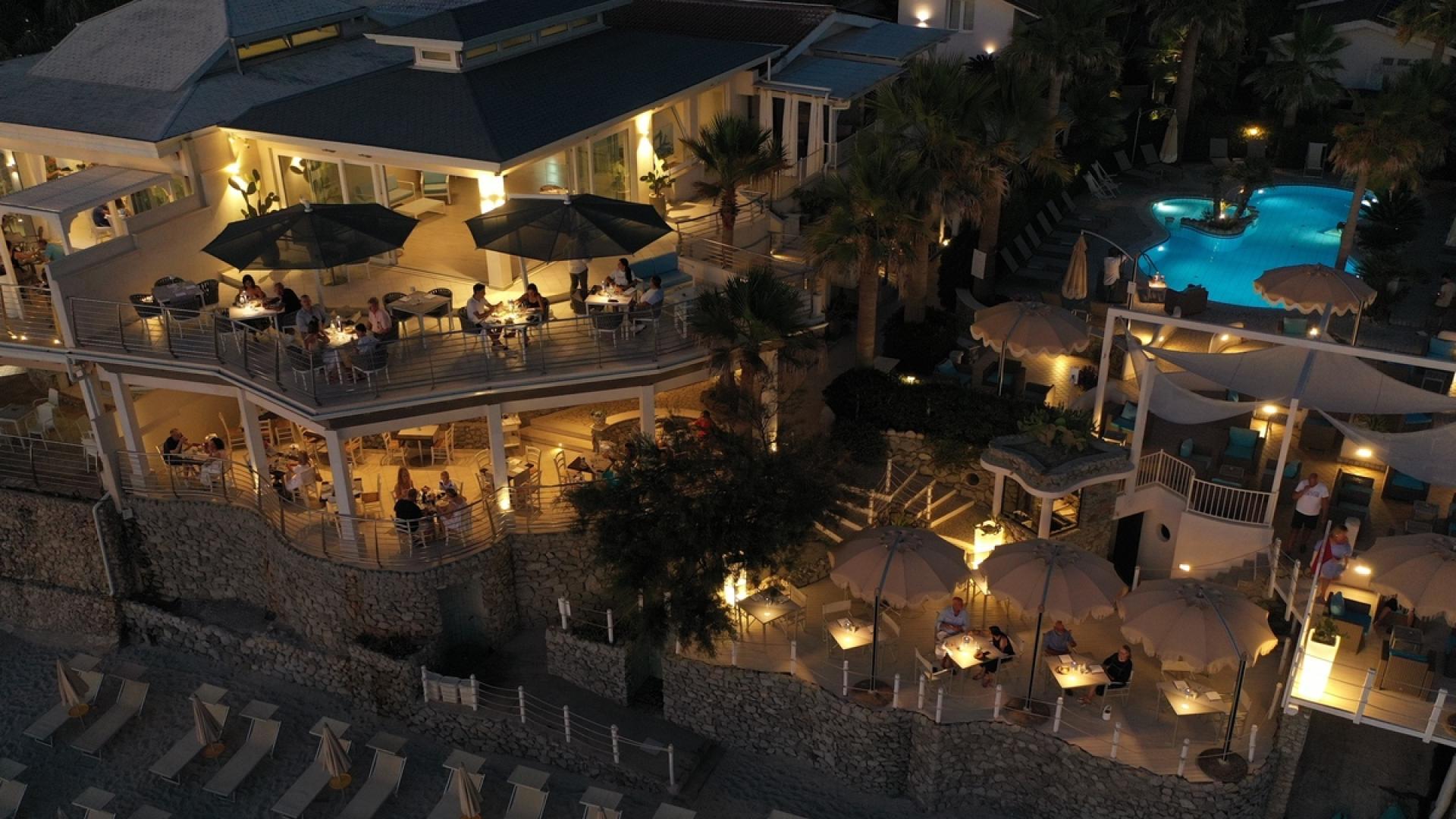 Ristorante sul mare con terrazza e piscina illuminata di notte.